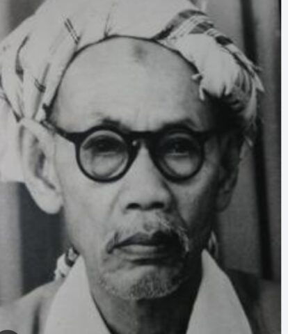 Portrait of Mahatma Gandhi wearing round glasses and a cloth on his head, looking thoughtful.